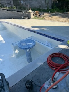 Custom mosaic tile pedestal table and sun shelf under construction with dark waterline tile