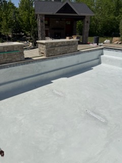 Freshly plastered pool shell before fill, with outdoor kitchen pavilion behind