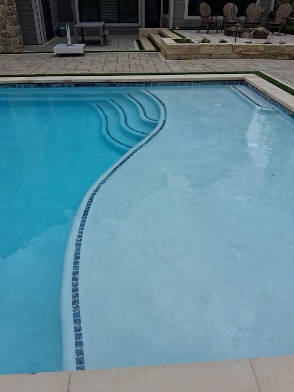Curved freeform pool with mosaic tile step accents and shallow lounging shelf