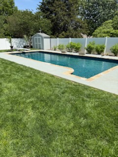 Pool and green lawn framed by white privacy fence in a finished backyard