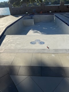 Lakeside pool nearing completion with tanning ledge and three-circle mosaic tile medallion in the deck