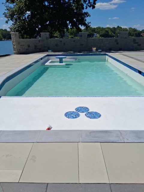 Lakeside rectangular pool with diving board, blue mosaic waterline tile and stone pillar wall